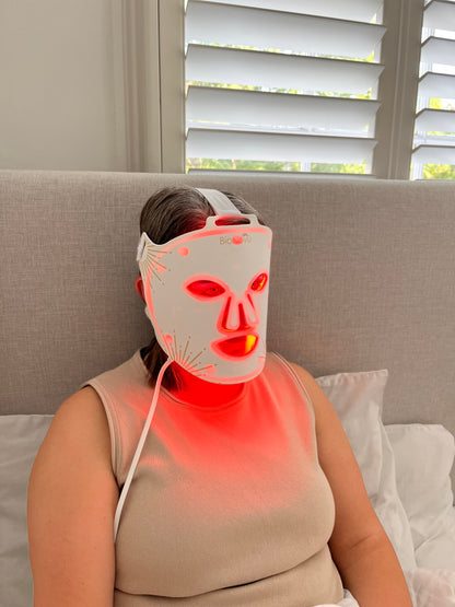 Person using a red light therapy device on their arm in a living room.